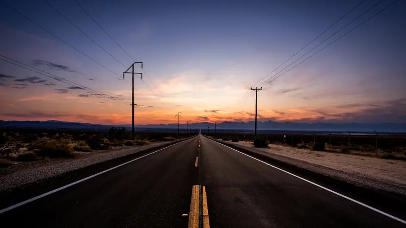 An empty highway stretching toward distant mountains under a golden sunset.