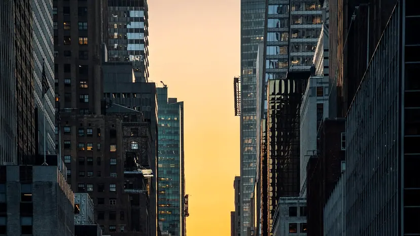 Cars filling a city avenue at sunset with the sun low between the buildings.