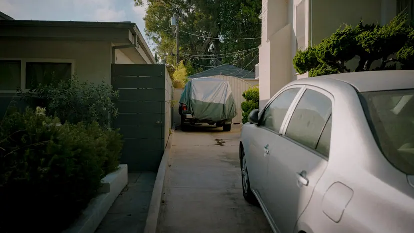 A car parked in a residential driveway beside a house in warm afternoon light.