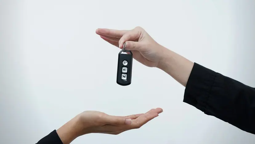 One hand passing a car key to another hand against a plain background.