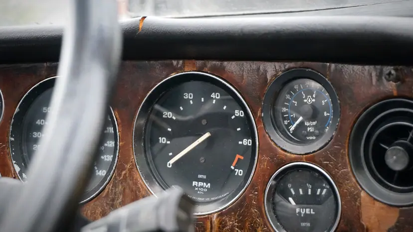 A close-up of analog instrument dials on a wood-trimmed car dashboard.