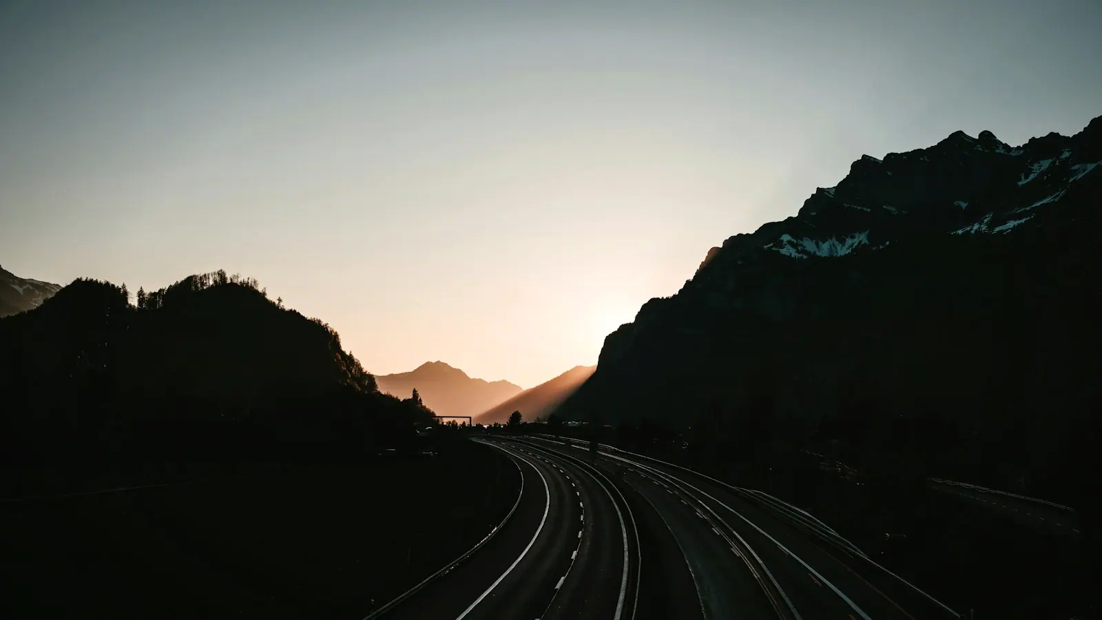 An empty mountain road curving toward the sunset between hillsides.